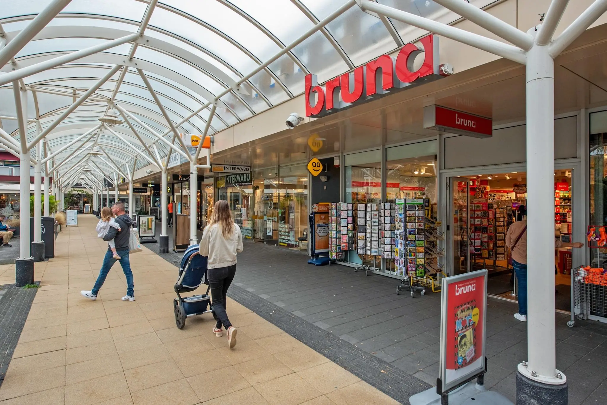 Winkelpassage aan de Koningin Julianalaan met mensen voor de Bruna en andere winkels.